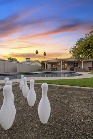 Un jardin avec une piscine, une terrasse dotée de mobilier d’extérieur et une vue sur le coucher de soleil.