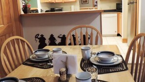 A dining area with a table set for four, wooden chairs, a kitchen in the background, and a decorative wall with silhouettes. - Notchtop Mountain Condo (Estes Park)