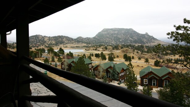A view from a balcony overlooking a mountainous landscape with several wooden cabins and a lake. - Notchtop Mountain Condo (Estes Park)