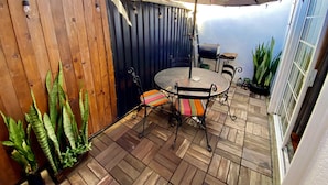 Een terras met een ronde tafel, stoelen, een houten hek en potplanten.