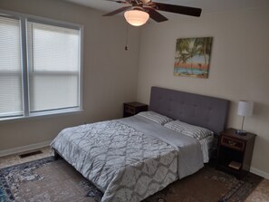 A bedroom with a bed, nightstands, a ceiling fan, a window with blinds, and a painting on the wall. - Large four bedroom (Macon)