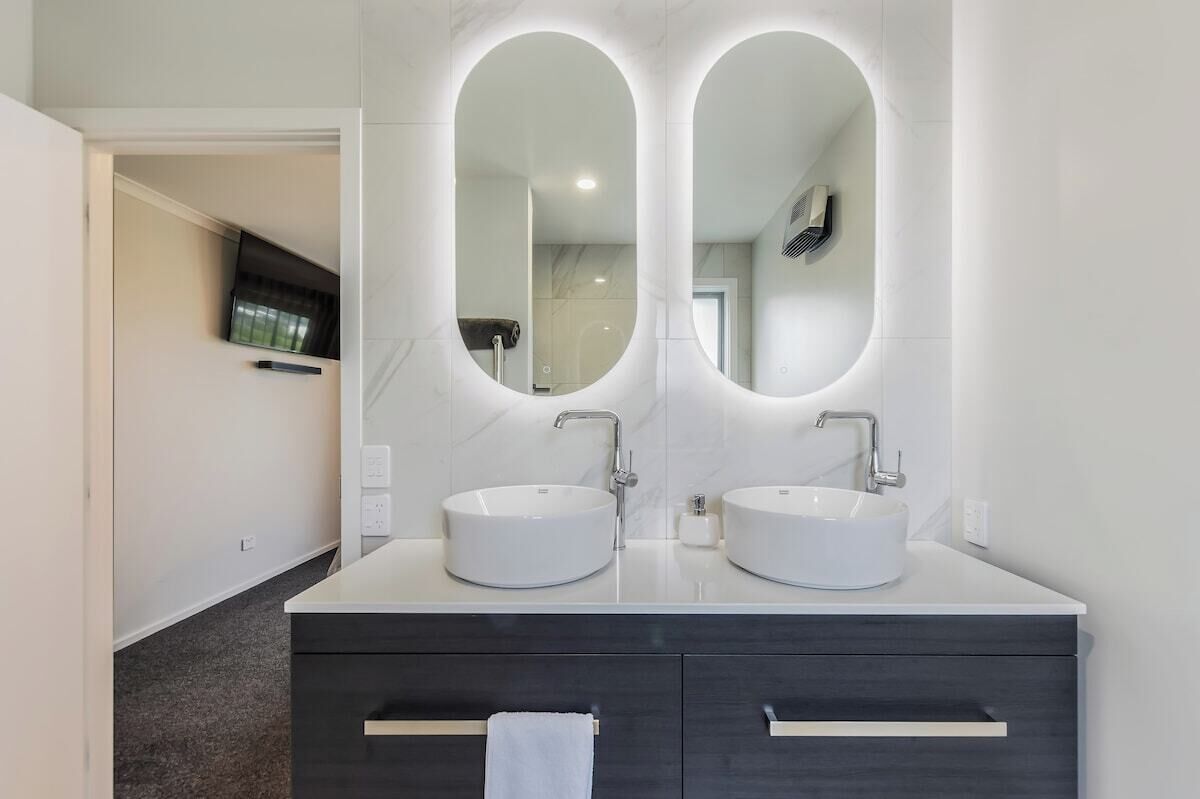 A modern bathroom with two round sinks, a large mirror, and dark cabinetry.