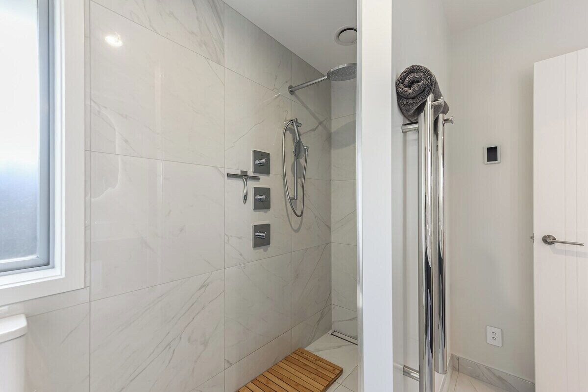 A modern bathroom with a glass-enclosed shower, a wooden bath mat, and a white door.