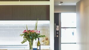 Une cuisine moderne dotée d’un îlot central, un coin repas avec une table et des chaises en bois, et un couloir lumineux menant à une autre pièce.