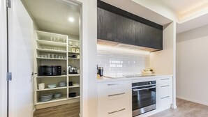 Une cuisine moderne avec des meubles blancs, un four encastré et un garde-manger contenant de la vaisselle et des verres.