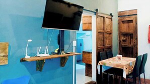 Ein Zimmer mit blauer Wand, einem an der Wand befestigten Flachbildfernseher, einem Holzregal mit elektronischen Geräten, einem Tisch mit Stühlen und einer Tür im rustikalen Stil.