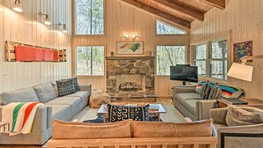 Un intérieur de chalet chaleureux avec une cheminée en pierre, des murs en bois et de grandes fenêtres.