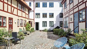 A courtyard with a cobblestone path, a seating area with chairs, and a building with a white facade and timber framing. - 2 bedroom awesome apartment in Ystad (Ystad)