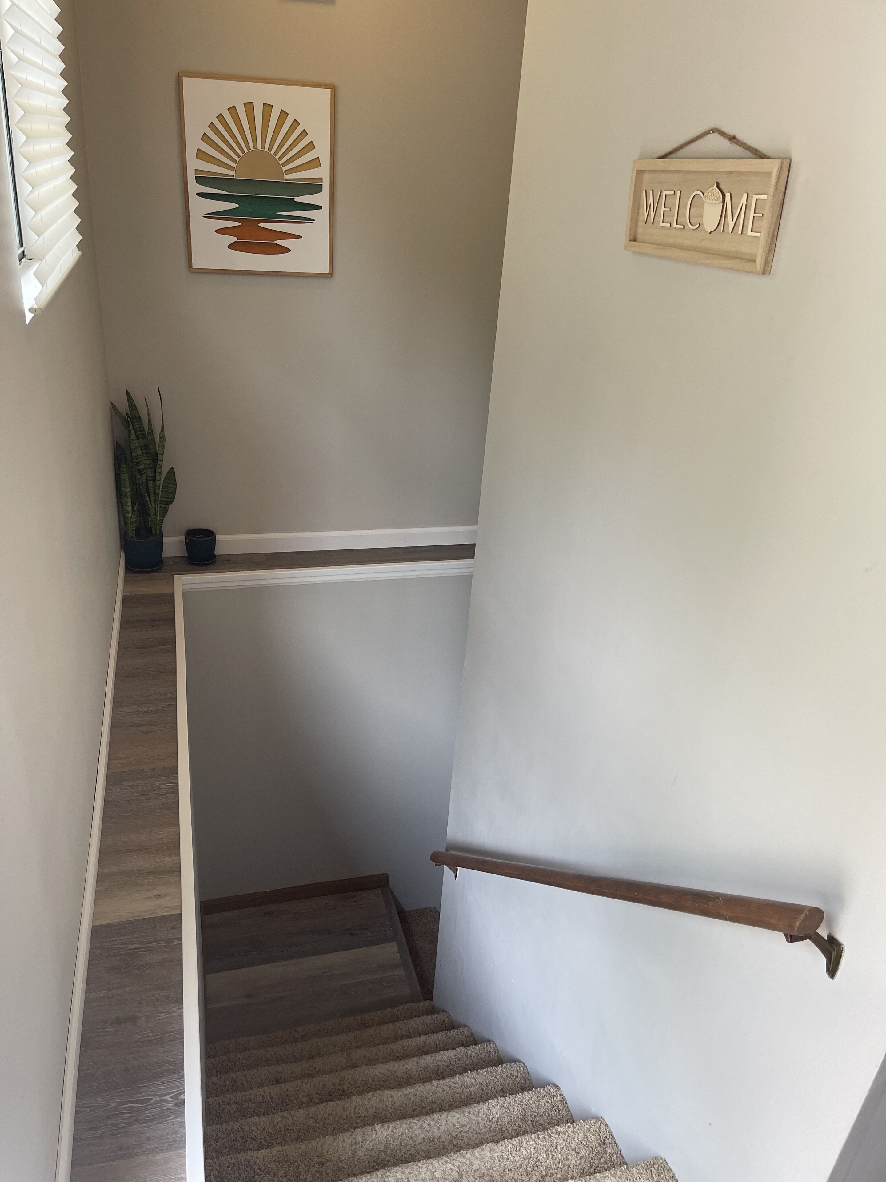 Een trap met een houten leuning, een welkomstbord en een lijst met kunst aan de muur.