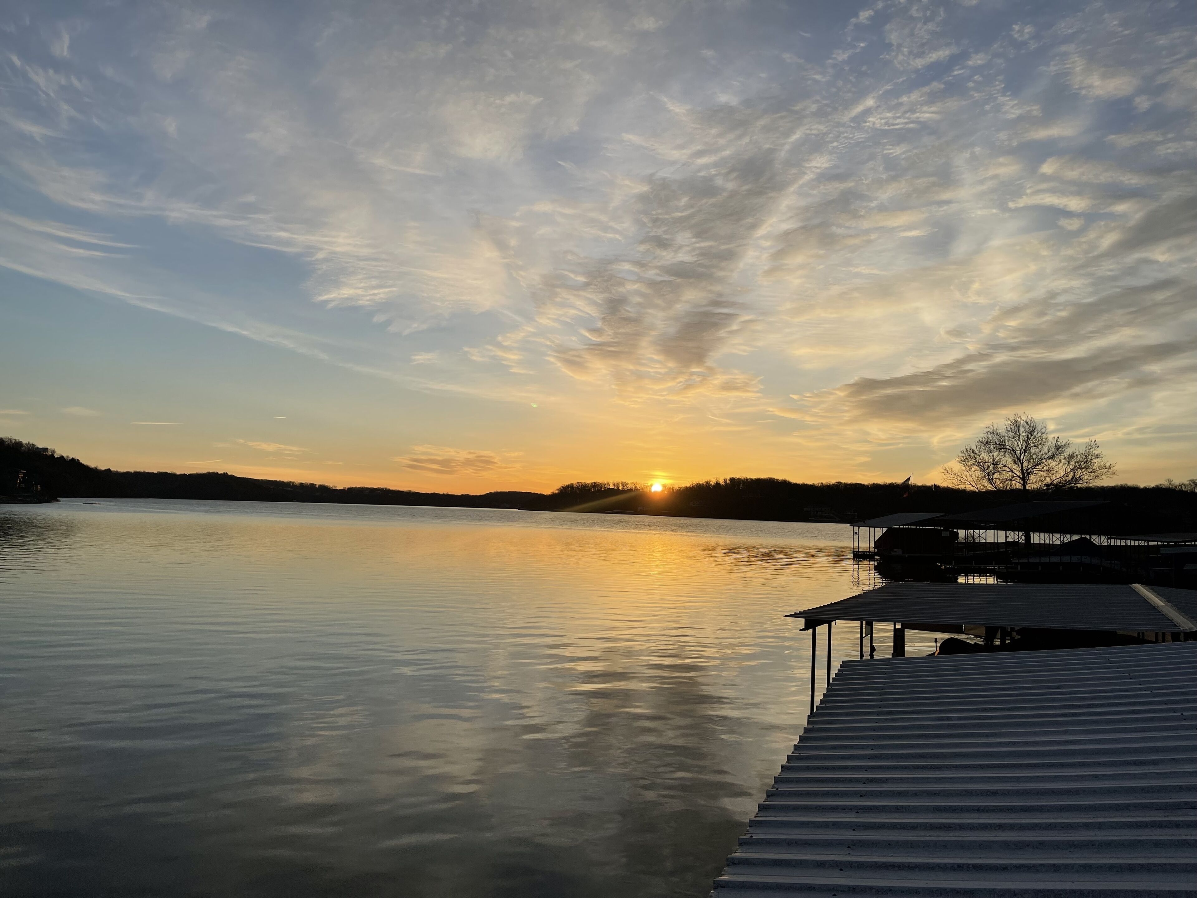 A calm lake at sunset with a dock extending into the water.
