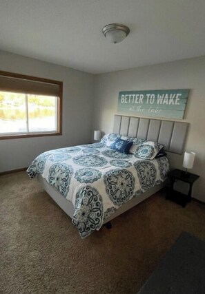 A bedroom with a bed, a window, a bedside table, and a wall sign.