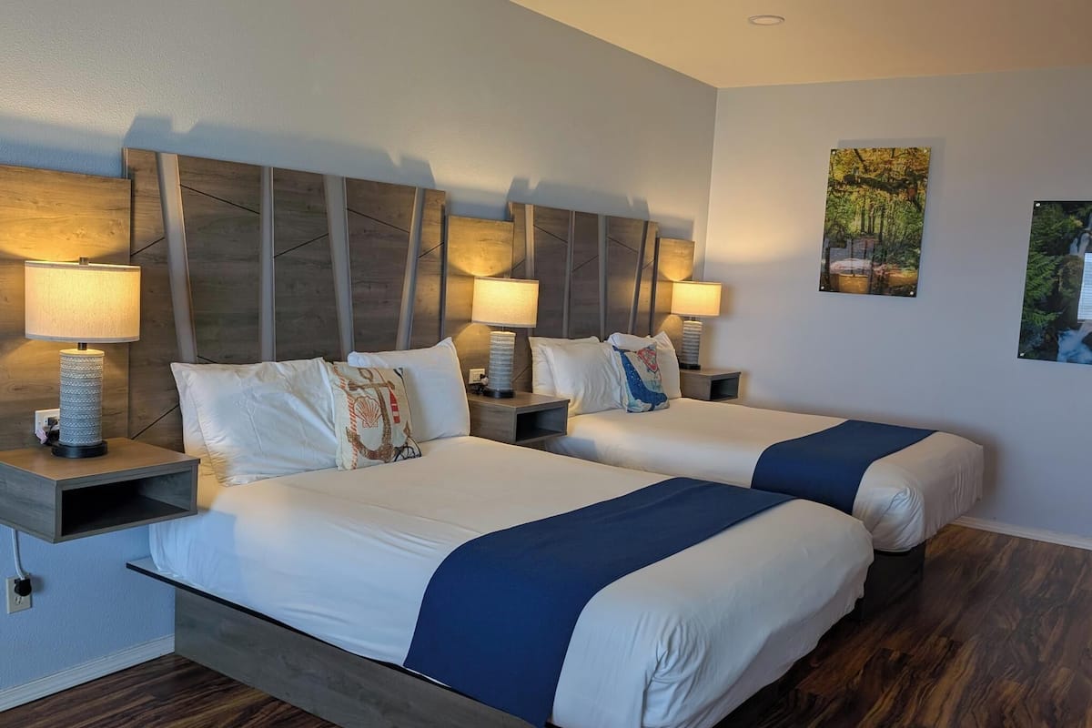 Une chambre d’hôtel avec deux lits, des têtes de lit en bois, des lampes de chevet et des œuvres d’art accrochées au mur.