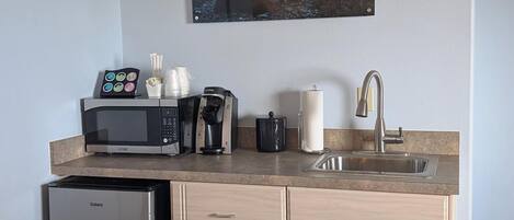 Et kompakt køkken med køleskab, mikrobølgeovn, kaffemaskine og vask.