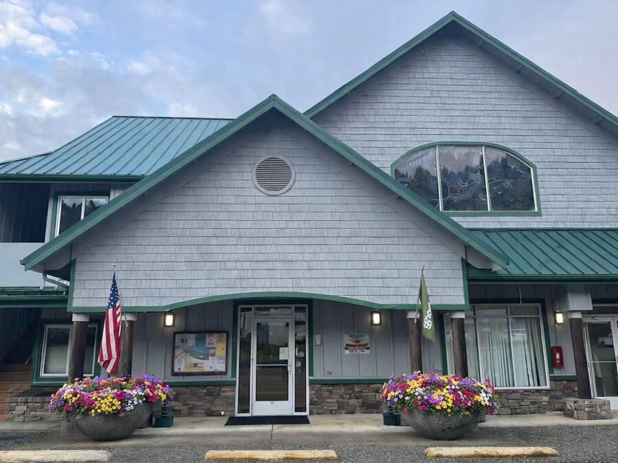 A two-story building with a green roof and a large entrance door. There are two flower planters in front of the entrance.
