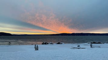 A snowy landscape with a body of water and a sunset in the background.
