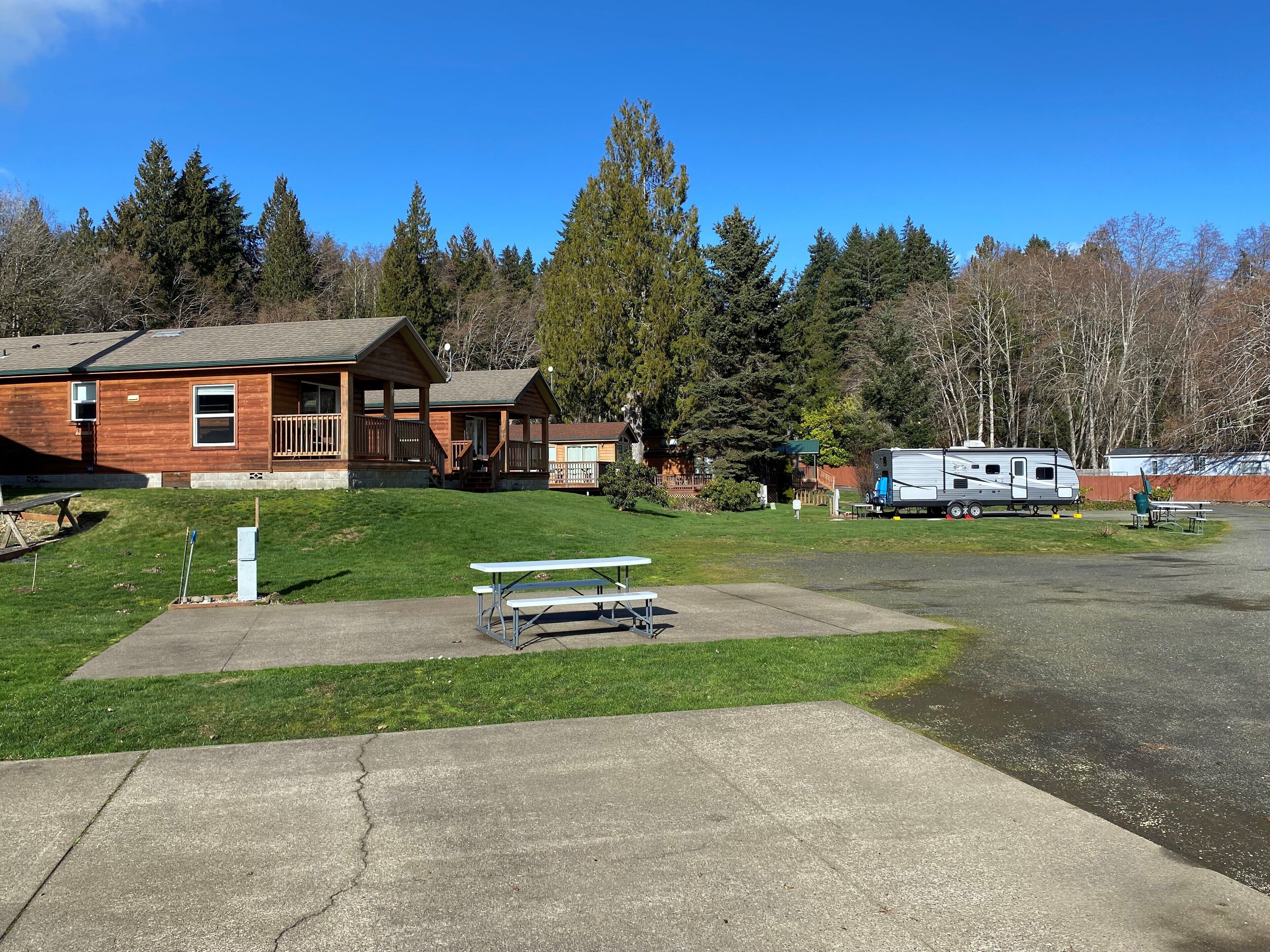 A lodge with a large deck and picnic tables, surrounded by trees and a clear sky.