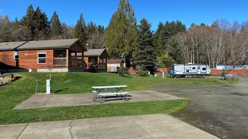 A lodge with a large deck and picnic tables, surrounded by trees and a clear sky.