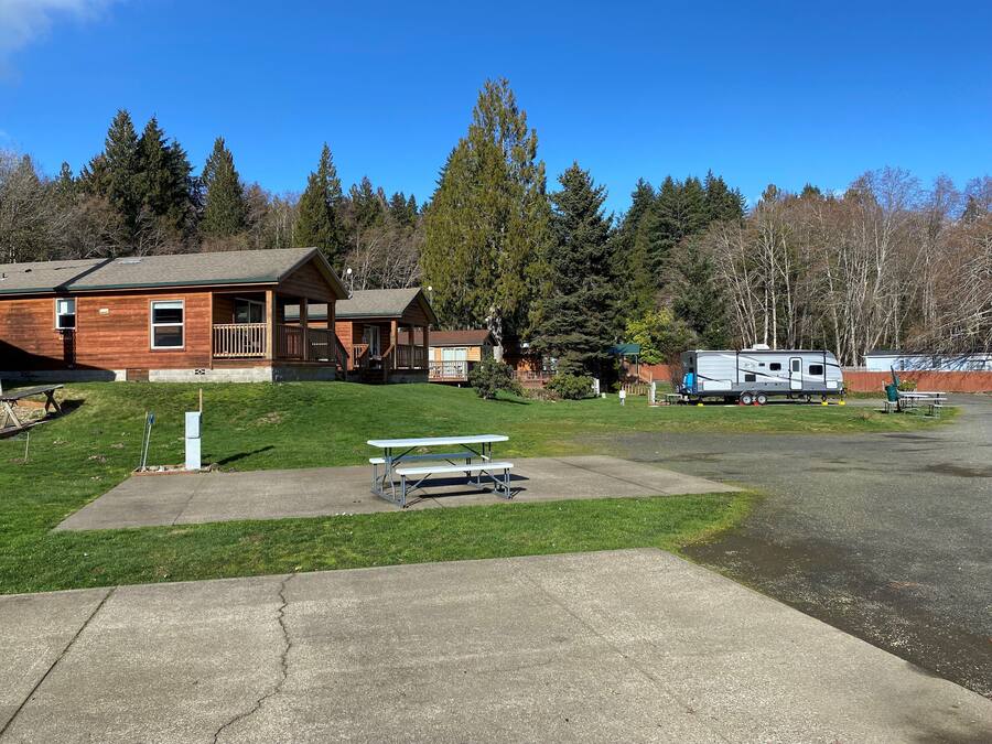 A lodge with a large deck and picnic tables, surrounded by trees and a clear sky.