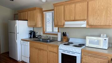 Una cocina con armarios de madera, un refrigerador blanco, una estufa, un microondas y una ventana con persianas.