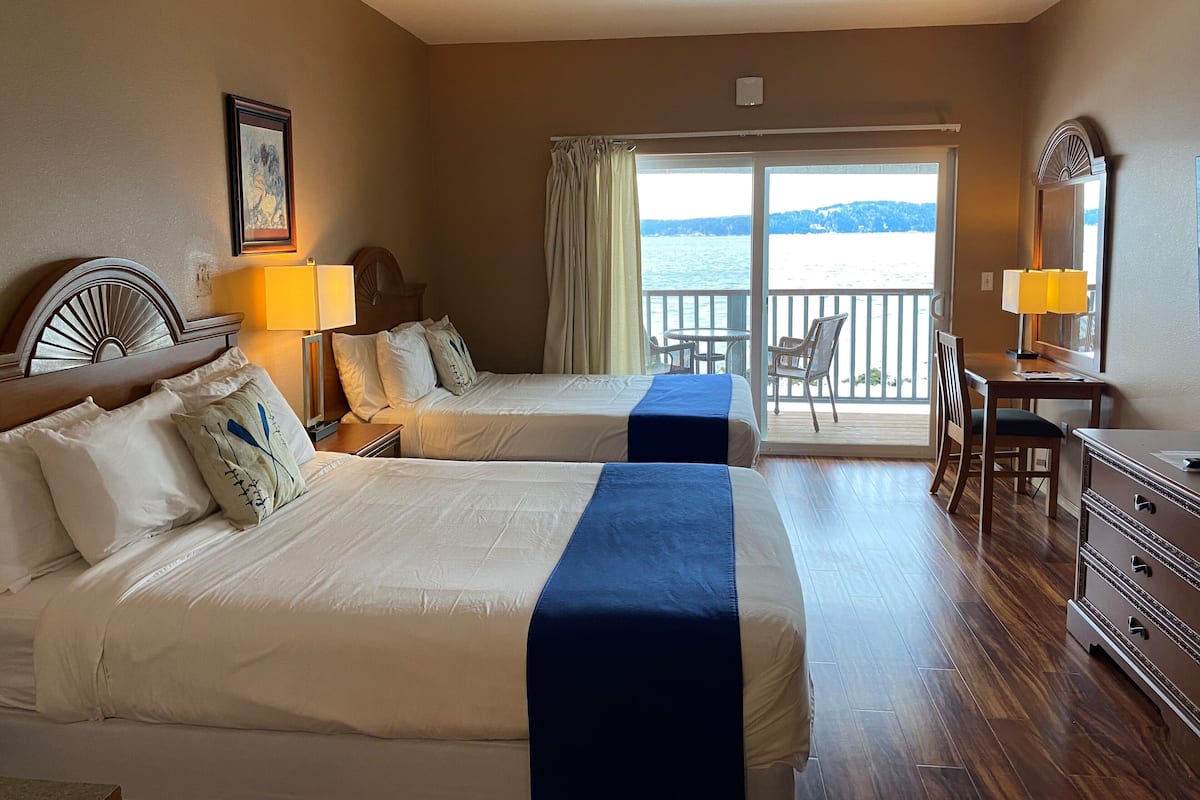 Une chambre d’hôtel avec deux lits, un bureau, une chaise et un balcon donnant sur l’eau.