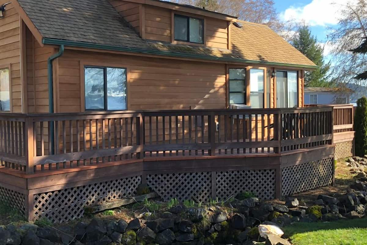 Une cabane en bois dotée d’une terrasse, de grandes fenêtres et de fondations en pierre.