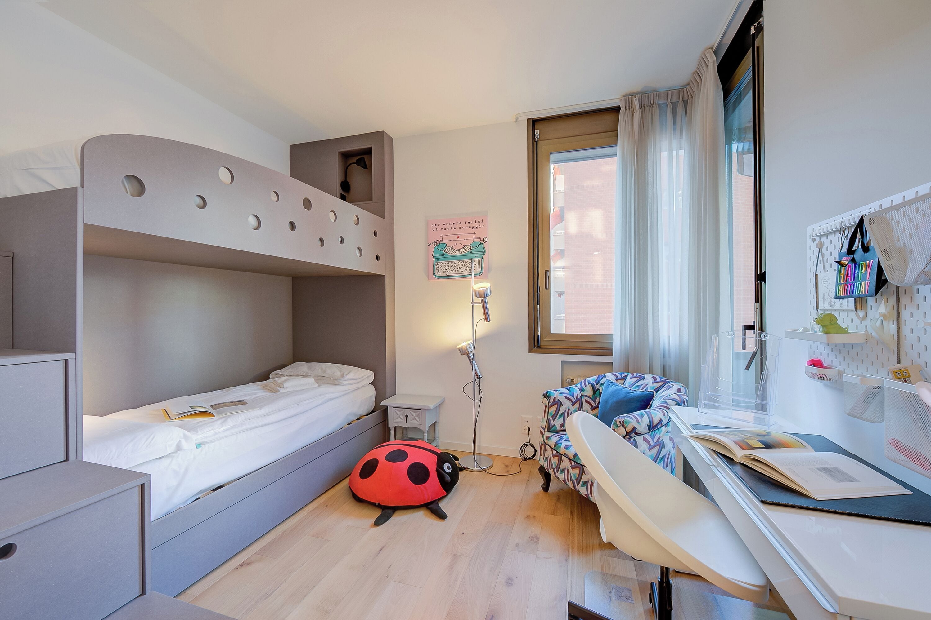 A compact room with a bunk bed, a desk with a chair, and a small bedside table.