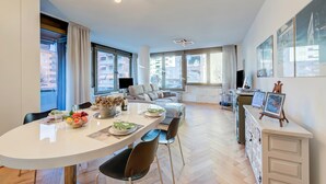 A modern living room with a sofa, a dining table with fruit, and a large window. - Dandy House Few Min From Lake (Lugano)