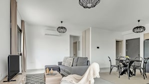 A modern living room with a grey sofa, a TV, and a dining area with a table and chairs. - Sanders Only - Cute 2-bdr Apt With Balcony (Limassol)
