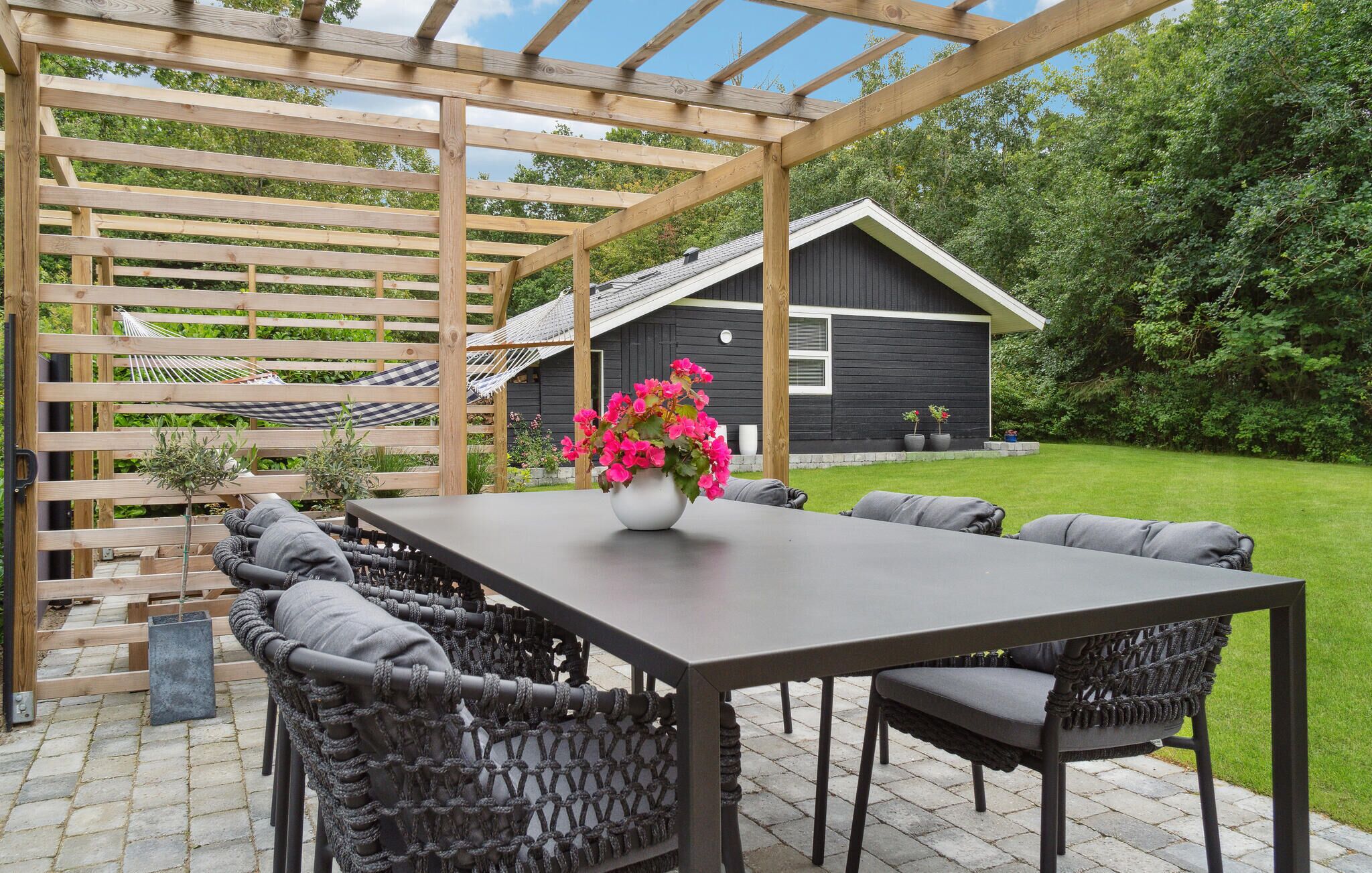 Eine überdachte Terrasse mit Tisch, Stühlen und einer Hängematte, mit Blick auf einen Garten.
