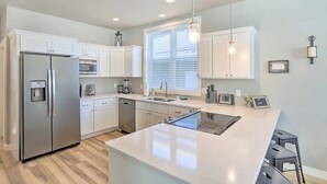 Una cocina moderna con armarios blancos, electrodomésticos de acero inoxidable, una isla central e iluminación colgante.