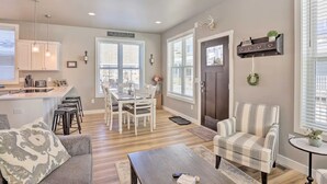 Una cocina moderna con armarios blancos, un comedor con mesa y sillas blancas, un sillón a rayas y una pequeña mesita auxiliar.