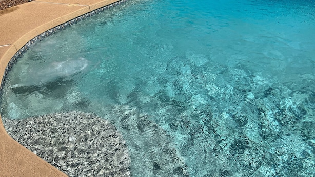Una piscina trasparente con bordo in pietra, circondata da lettini e un piccolo tavolino.