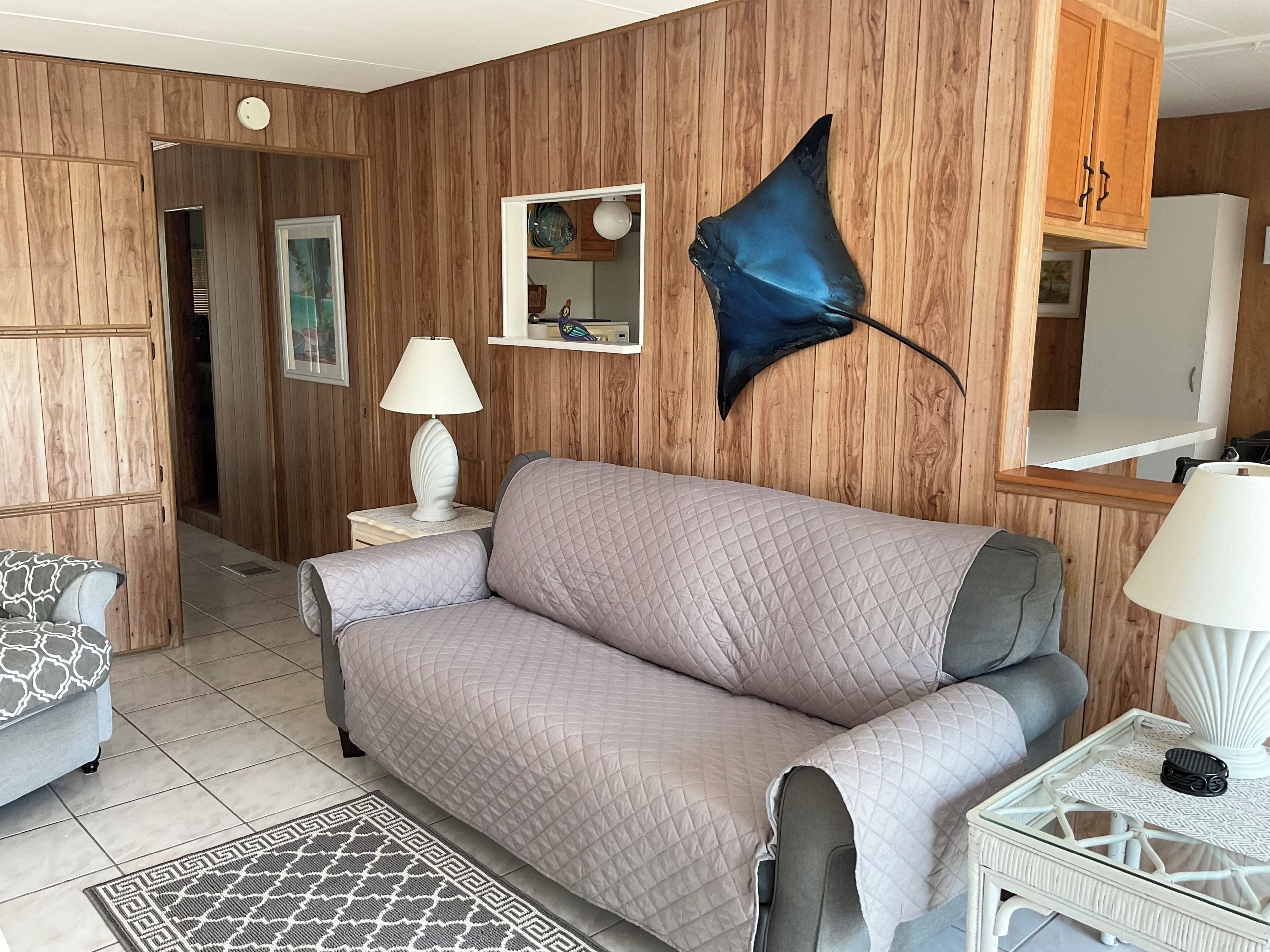 A room with a wooden wall panel, a sofa, a small table with a lamp, and a decorative fish on the wall.