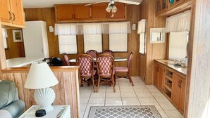 A compact kitchen with wooden cabinets, a dining table with chairs, a white lamp, and a patterned rug. - ISLE BE BACK To The Sunny Keys (Cudjoe Key)