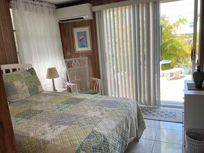 A bedroom with a bed, a chair, a table, and a view of the outside.