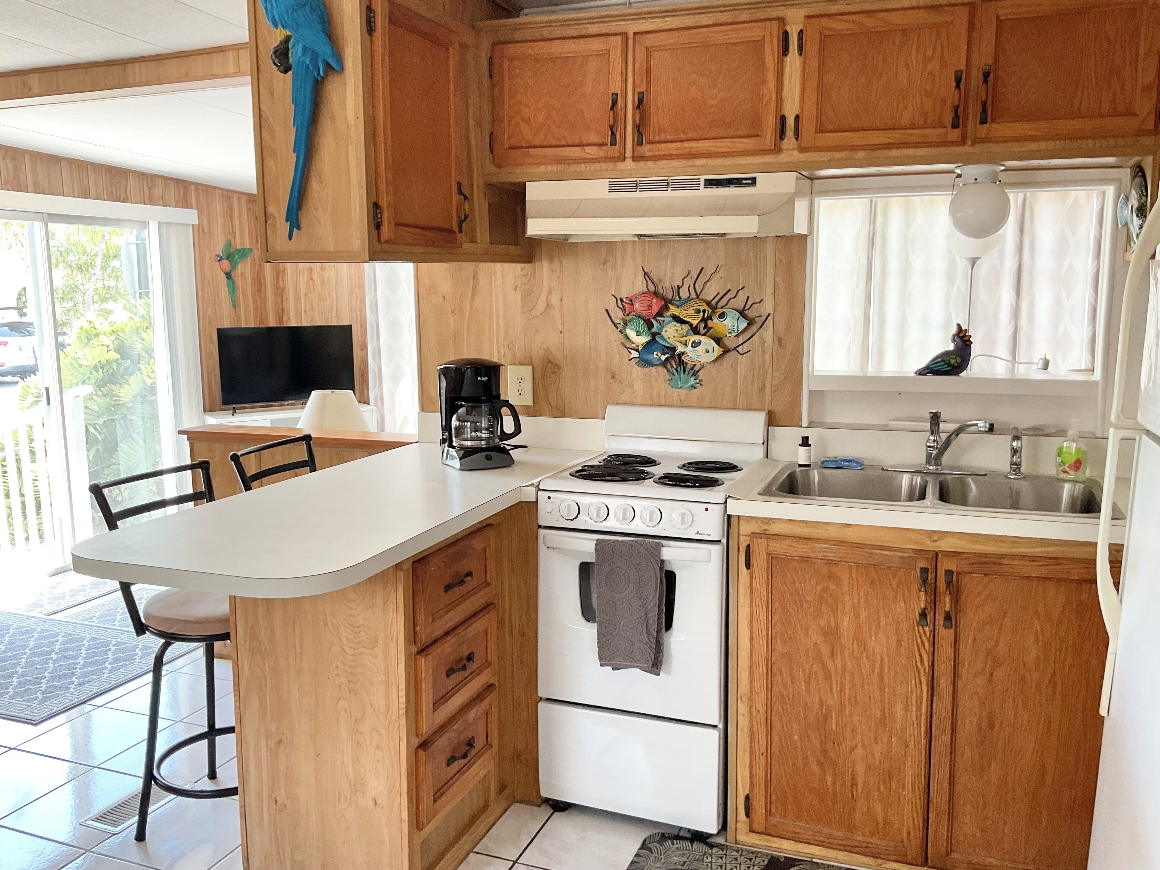 A kitchen with wooden cabinets, a white countertop, a stove, a sink, and a decorative fish wall art.