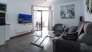 Ett modernt vardagsrum med ett soffbord med glasskiva, en grå soffa, en platt-TV och en tavla som föreställer en stadsbild.