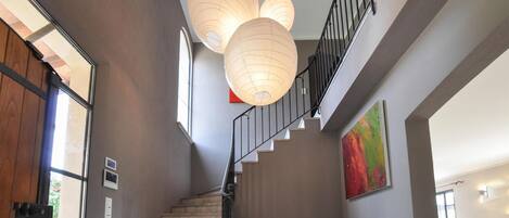A staircase with a wooden handrail and a metal railing, leading to a landing with a wooden chair and a colorful painting.