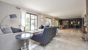 A spacious living area with a sofa set, a round coffee table, and a dining table with chairs. There are large windows providing natural light and a view of the outdoors. - Stunning home in Fayence with sauna (Fayence)