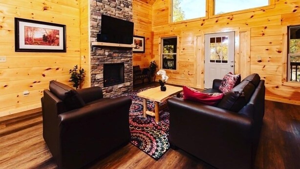 Interior acogedor de una cabaña con chimenea de piedra, paredes de madera, televisor de pantalla plana y un ventanal grande.