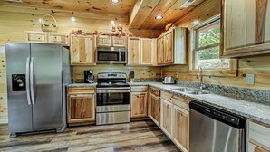 Una cocina moderna con armarios de madera, electrodomésticos de acero inoxidable, encimeras de granito y un ventanal que proporciona luz natural.