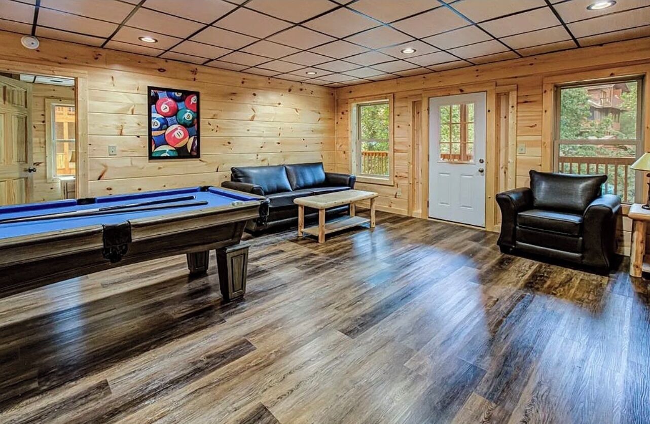 A wooden interior with a pool table, a leather sofa, and a chair.