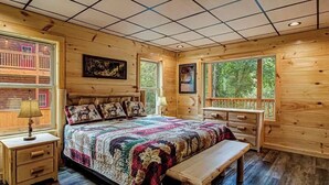 Un dormitorio acogedor con una cama grande, paredes de madera, un banco y una ventana con vista a árboles.