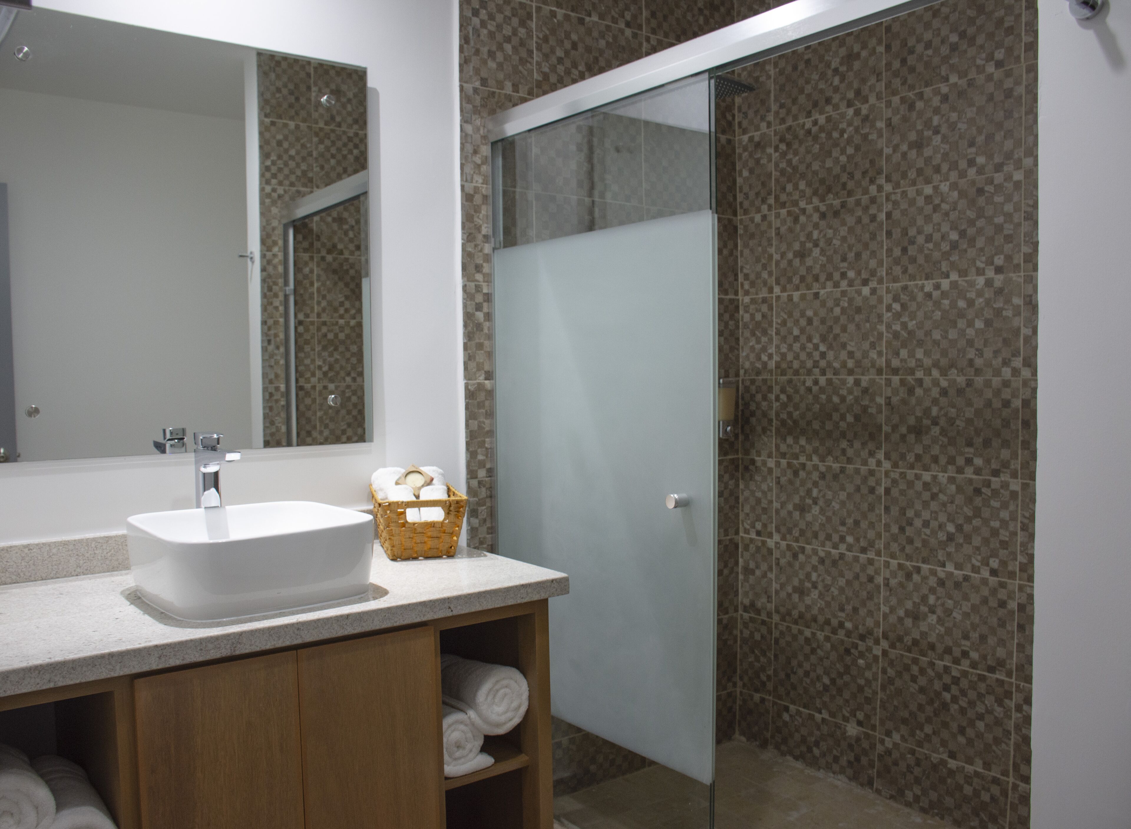 Un baño moderno con un espejo grande, un lavabo blanco, una cabina de ducha con mampara de cristal y un mueble de tocador de madera con toallas.