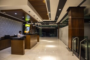 Un hall d’hôtel moderne avec un comptoir d’accueil, un mur orné de motifs géométriques et un mur d’accent en bois.