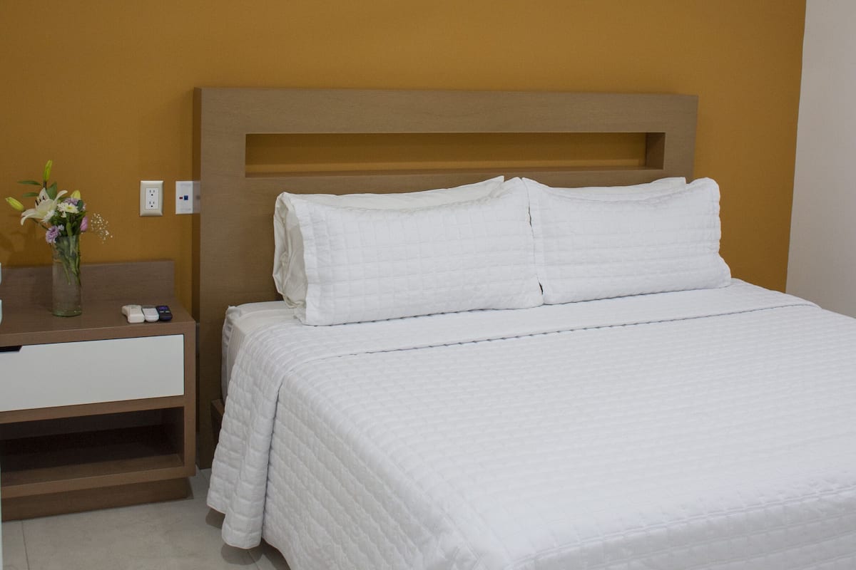 Quarto de hotel com uma cama, mesa de cabeceira, um vaso de flores e um ventilador de teto.