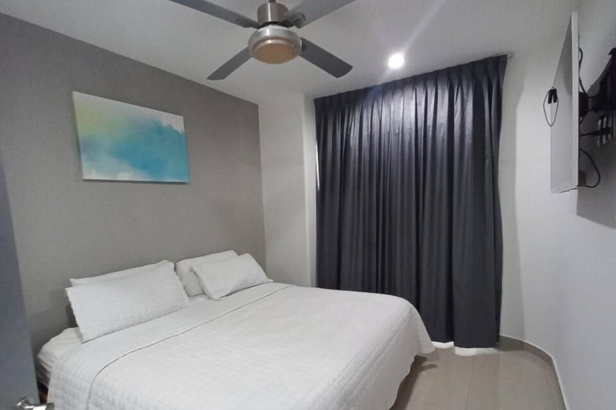 Quarto com cama, ventilador de teto, pintura e janela com cortinas.