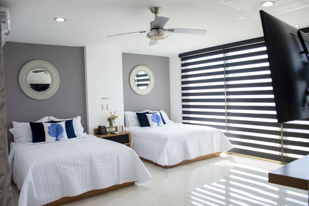Quarto de hotel com duas camas, um ventilador de teto, um espelho grande e uma televisão.