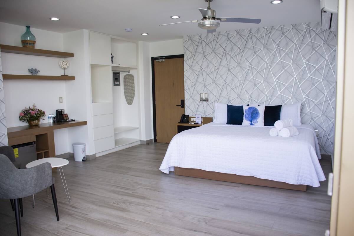 Quarto moderno com cama, mesa de cabeceira e área de trabalho.