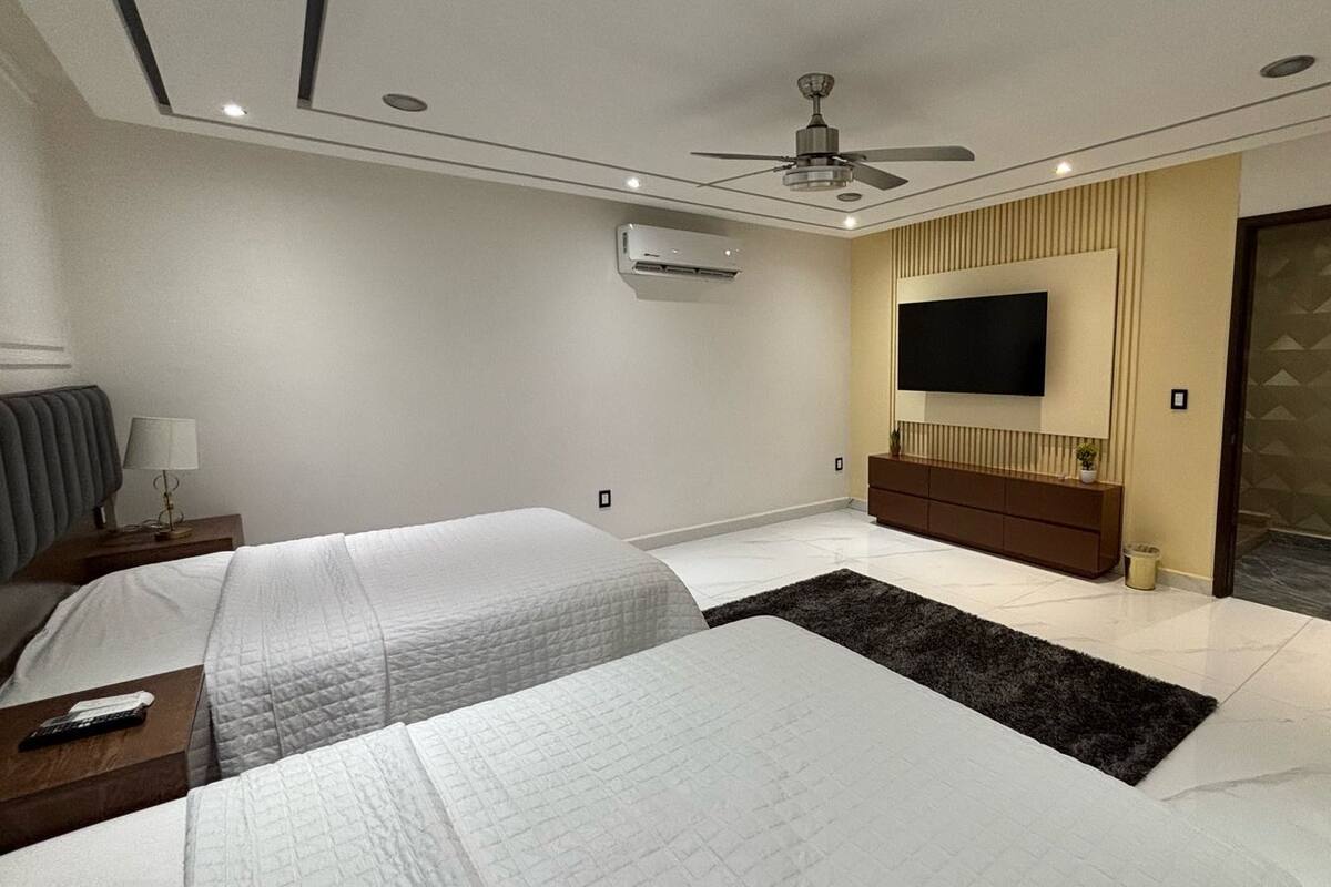 Quarto de hotel moderno com duas camas, televisão de tela plana, ventilador de teto e uma janela grande.